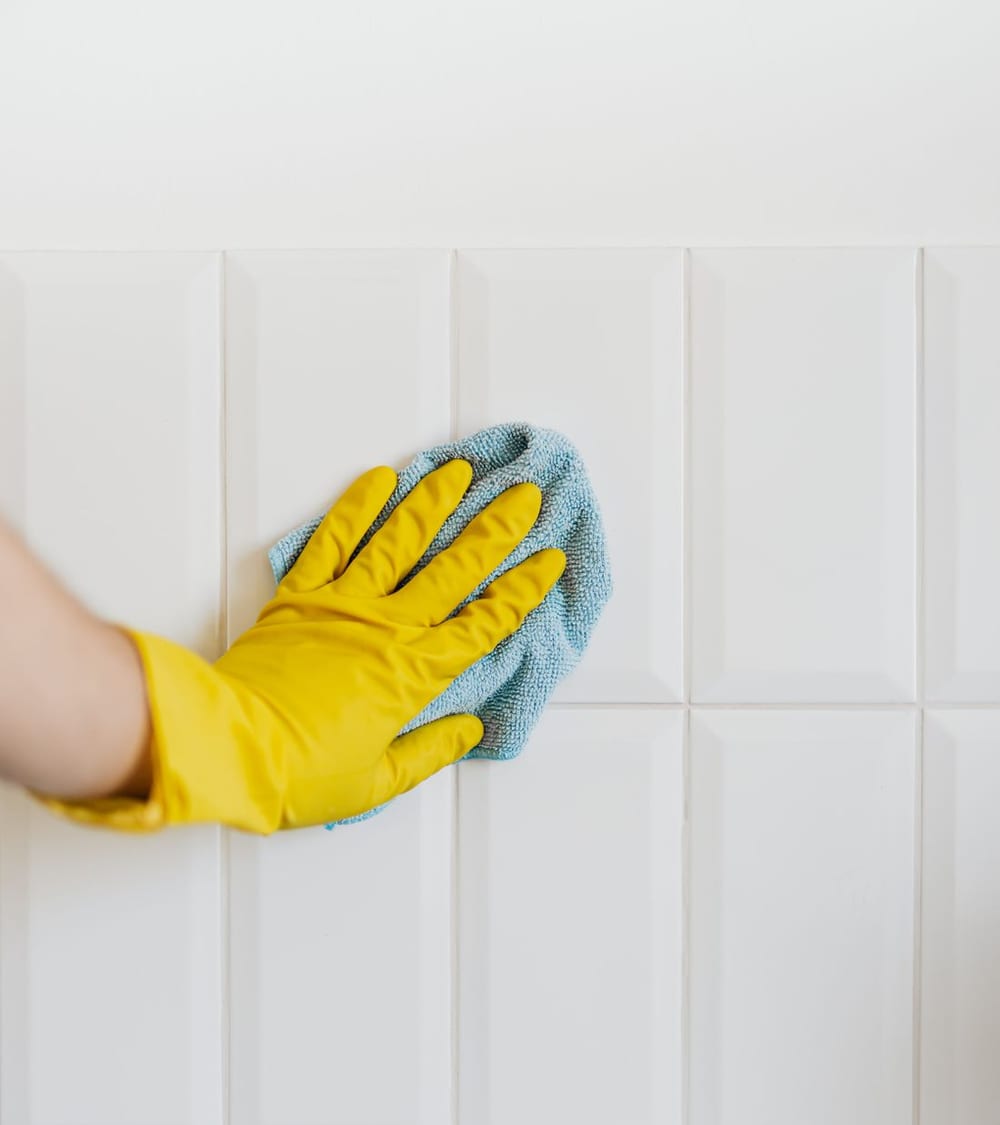 Main gantée nettoyant des carreaux blancs avec une microfibre