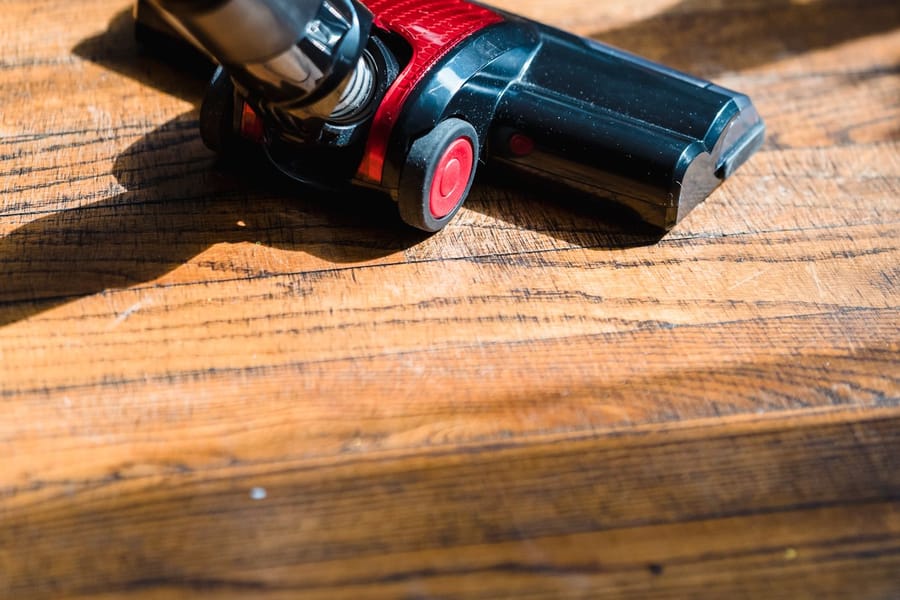 Aspirateur passant sur un parquet en bois clair ensoleillé